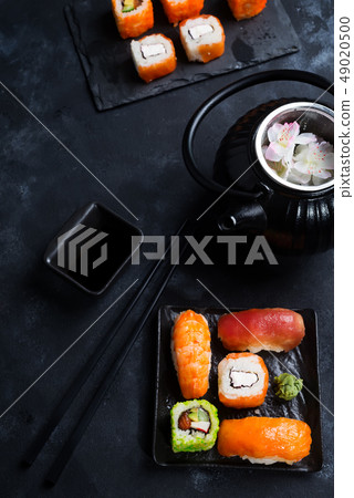 Asian food background with black iron teapot and sushi set on slate plate on black stone table, flat Asian food background with black iron teapot and sushi set on slate plate on black stone table, flat 49020500
