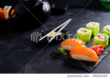Asian food background with black iron teapot and sushi set on slate plate on black stone table 49020506