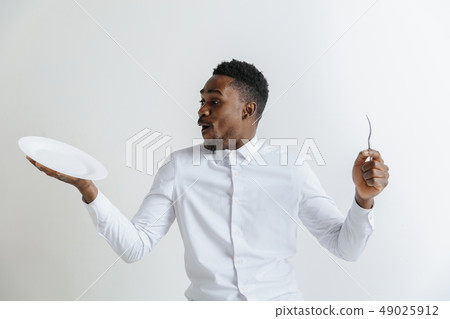 Young surprised attractive african american guy holding empty dish and fork isolated on grey 49025912
