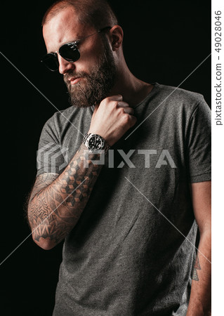 Portrait of a handsome balded man with long well trimmed beard wearing sunglasses and grey shirt 49028046