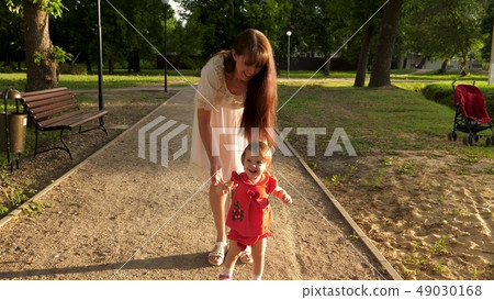 child learns to walk along path in park in summer, mother walks with the baby 49030168
