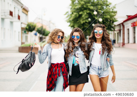Tredny smiling girlfriends walking along the 49030680
