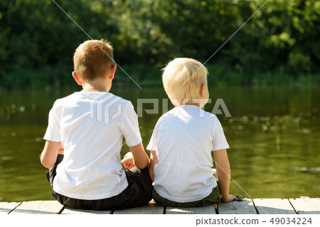 Two little boys are sitting on the pier on the 49034224