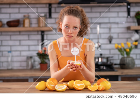 Skinny woman leaning on kitchen table and carrying half of lemon 49040690