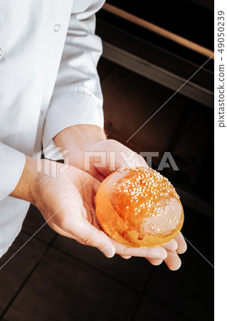 Top view of little bun topped with sesame seeds in hands of baker Top view of little bun topped with sesame seeds in hands of baker 49050239
