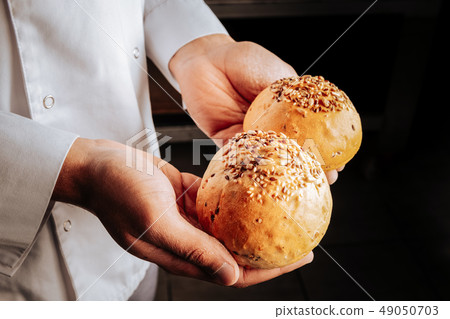 Baker wearing white jacket holding two little buns Baker wearing white jacket holding two little buns 49050703