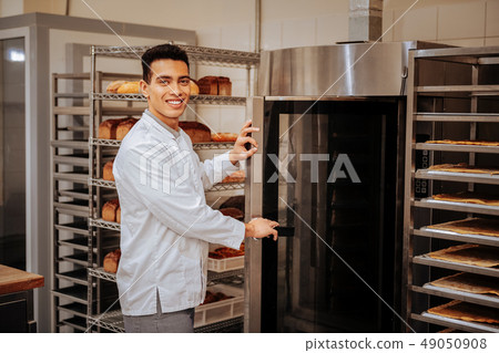Pleasant baker standing near big oven in the kitchen 49050908