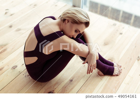 Short-haired woman in violet outfit grabbing her foot with both hands 49054161