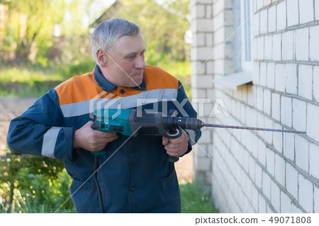 male builder drills brick wall with a perforator male builder drills brick wall with a perforator 49071808