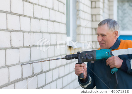 male builder drills brick wall with a perforator male builder drills brick wall with a perforator 49071818
