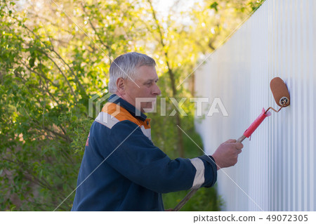 man paints a white metal fence with a roller man paints a white metal fence with a roller 49072305