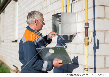 specialist man repairs a gas meter hanging specialist man repairs a gas meter hanging 49072415