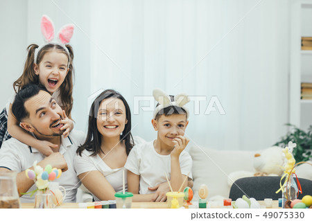 Happy family sitting at the table full of easter supplies, daughter is hugging her father. Father 49075330