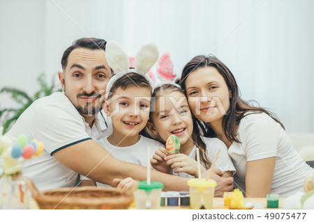 Happy family sitting at the table full og easter supplies, hugging and smiling. Children in funny Happy family sitting at the table full og easter supplies, hugging and smiling. Children in funny 49075477