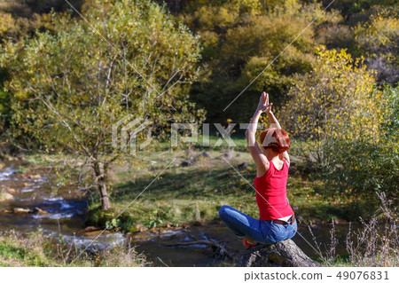 Young woman sits on a stone and meditates Young woman sits on a stone and meditates 49076831