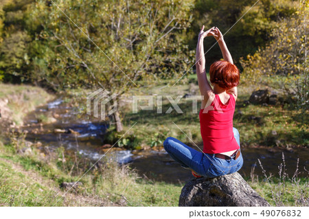 Young woman sits on a stone and meditates Young woman sits on a stone and meditates 49076832