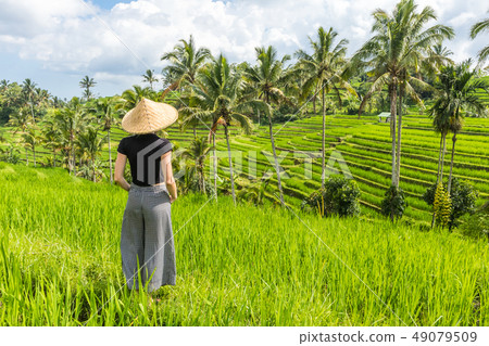 Relaxed fashionable caucasian female tourist wearing small backpack and traditional asian paddy hat Relaxed fashionable caucasian female tourist wearing small backpack and traditional asian paddy hat 49079509