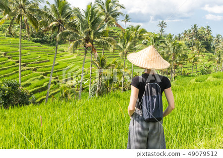 Relaxed fashionable caucasian female tourist wearing small backpack and traditional asian paddy hat Relaxed fashionable caucasian female tourist wearing small backpack and traditional asian paddy hat 49079512