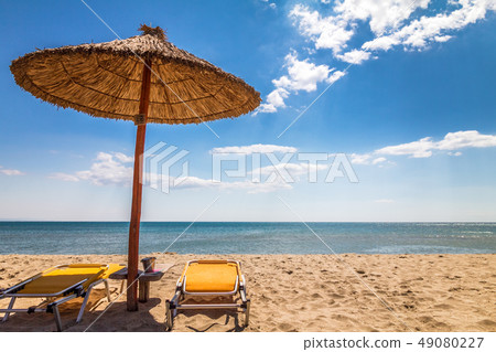 A straw umbrella with deck chairs on a sandy beach A straw umbrella with deck chairs on a sandy beach 49080227