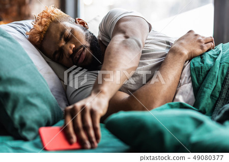 Nice good looking sleepy man taking his smartphone 49080377