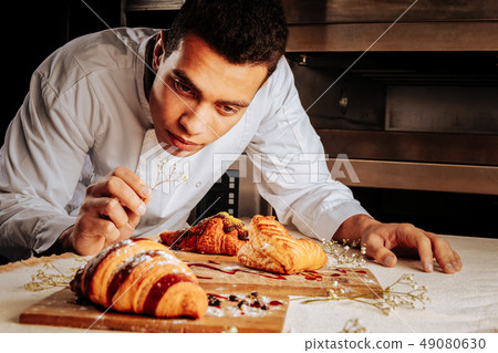 Baker leaning on table and looking at amazing desserts 49080630