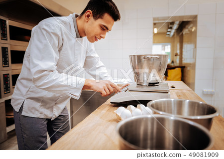 Baker wearing white jacket using modern kitchen scales Baker wearing white jacket using modern kitchen scales 49081909