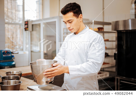 Experienced baker wearing white jacket standing near kitchen scale 49082044