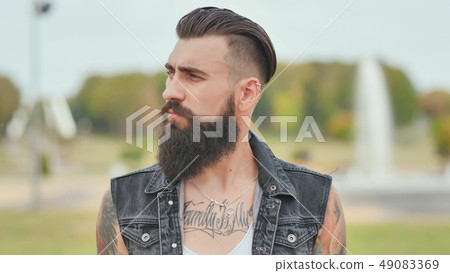 Portrait of a brutal and bearded man with tattoos on his shoulders. Portrait of a brutal and bearded man with tattoos on his shoulders. 49083369