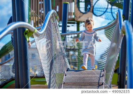 Sweet blond little baby girl in beautiful knitted dress plays outdoors at playground Sweet blond little baby girl in beautiful knitted dress plays outdoors at playground 49092835