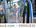 Sweet blond little baby girl in beautiful knitted dress plays outdoors at playground 49092836