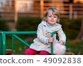 Portrait of sweet blond little baby girl in trench coat and faux fur bag at playground 49092838