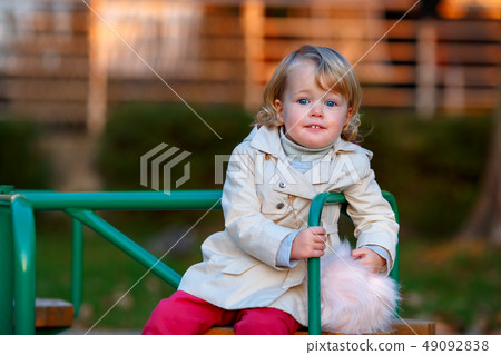 Portrait of sweet blond little baby girl in trench coat and faux fur bag at playground Portrait of sweet blond little baby girl in trench coat and faux fur bag at playground 49092838