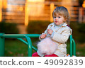 Portrait of sweet blond little baby girl in trench coat and faux fur bag at playground 49092839