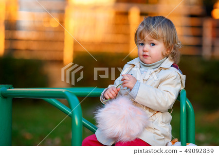 Portrait of sweet blond little baby girl in trench coat and faux fur bag at playground Portrait of sweet blond little baby girl in trench coat and faux fur bag at playground 49092839