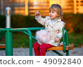 Portrait of sweet blond little baby girl in trench coat and faux fur bag at playground 49092840