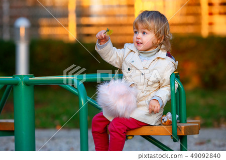 Portrait of sweet blond little baby girl in trench coat and faux fur bag at playground Portrait of sweet blond little baby girl in trench coat and faux fur bag at playground 49092840