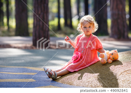 Sweet blond little baby girl in beautiful apricot dress plays walks outdoors at playground 49092841