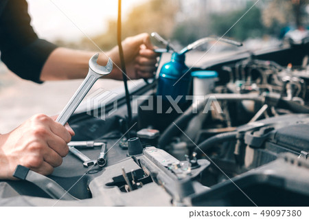 Asian car mechanic holds a wrench and a bottle of Asian car mechanic holds a wrench and a bottle of 49097380