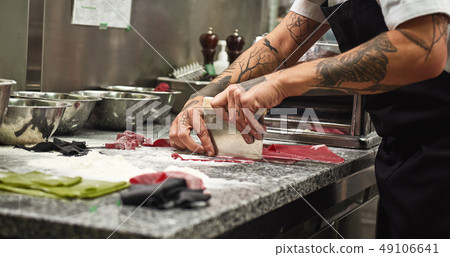 Making pasta process. Close up photo of chef's hands with tattoos cutting dough on the table with Making pasta process. Close up photo of chef's hands with tattoos cutting dough on the table with 49106641