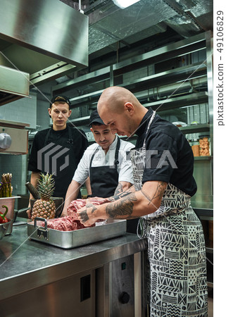 Culinary school. Professional chef with tattoos on his hands holding a red meat and teaching Culinary school. Professional chef with tattoos on his hands holding a red meat and teaching 49106829