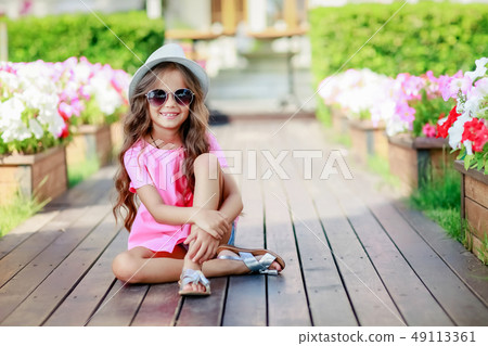 Fashion little girl model wearing a pink checkered shirt, hat and sunglasses in city Fashion little girl model wearing a pink checkered shirt, hat and sunglasses in city 49113361