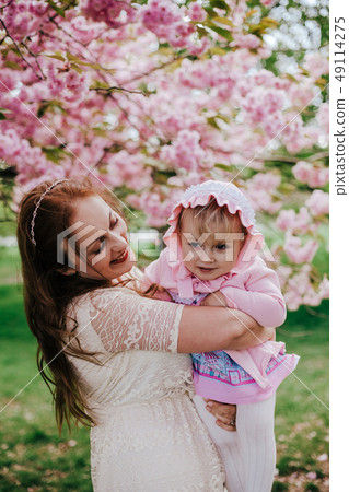 Loving mother and baby girl on background blooming pink flowers of cherry tree at springtime Loving mother and baby girl on background blooming pink flowers of cherry tree at springtime 49114275