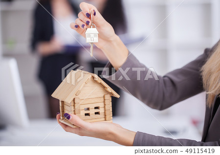Salesman carrying a model house in hand is delivering the house key to the buyer,Customers receive 49115419