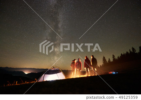 Friends resting beside camp, campfire under night starry sky Friends resting beside camp, campfire under night starry sky 49125359