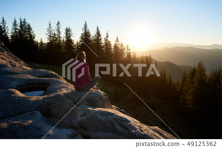 Woman hiker sitting on boulder in the mountains at sunset 49125362