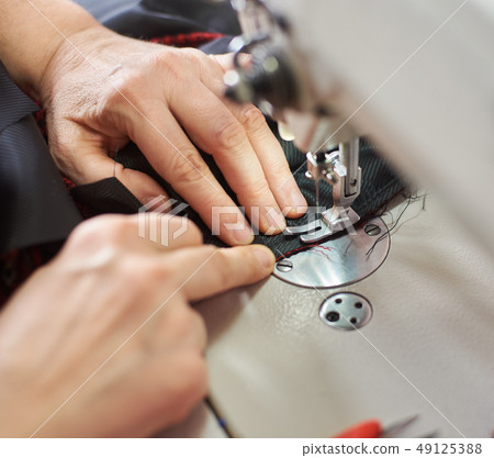 Female hands at sewing process and repairing plaid fabric on professional manufacturing machine 49125388