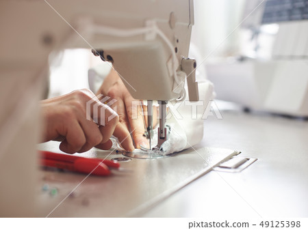 Female hands at sewing process and repairing white fabric on professional manufacturing machine 49125398