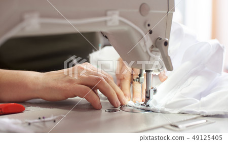 Female hands at sewing process and repairing white fabric on professional manufacturing machine Female hands at sewing process and repairing white fabric on professional manufacturing machine 49125405