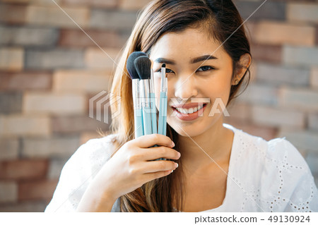 Young positive woman showing make-up brushes Young positive woman showing make-up brushes 49130924