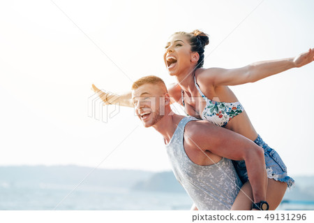 Cheerful boyfriend carrying girlfriend on his back 49131296
